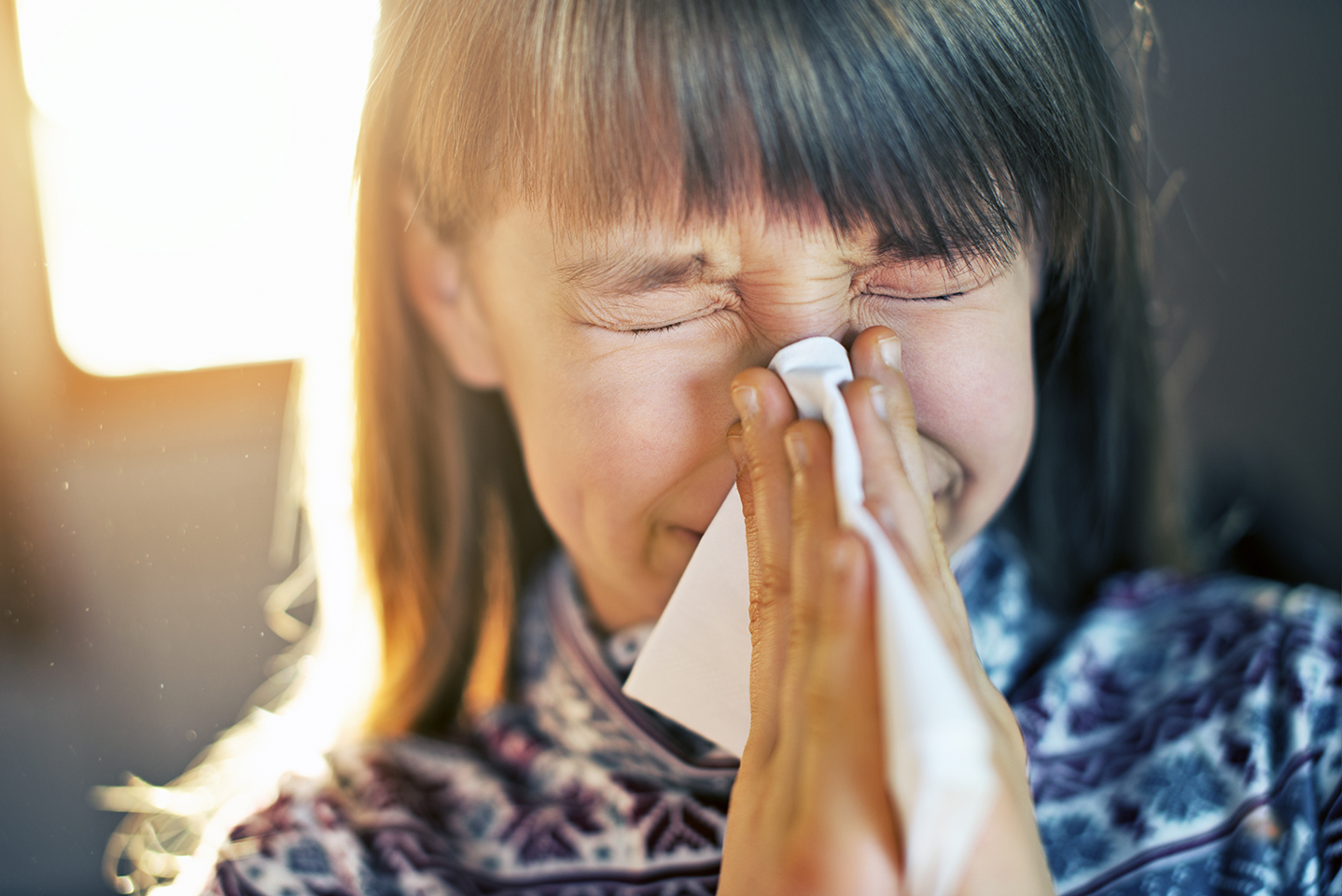 Little girl in dusty home cleaning nose. Dust particles visible in sun rays. The girl aged 9 cleaning her runny nose with a tissue.