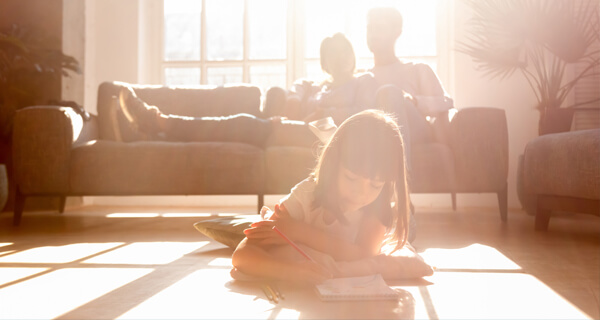 little girl writing in notebook at home with family