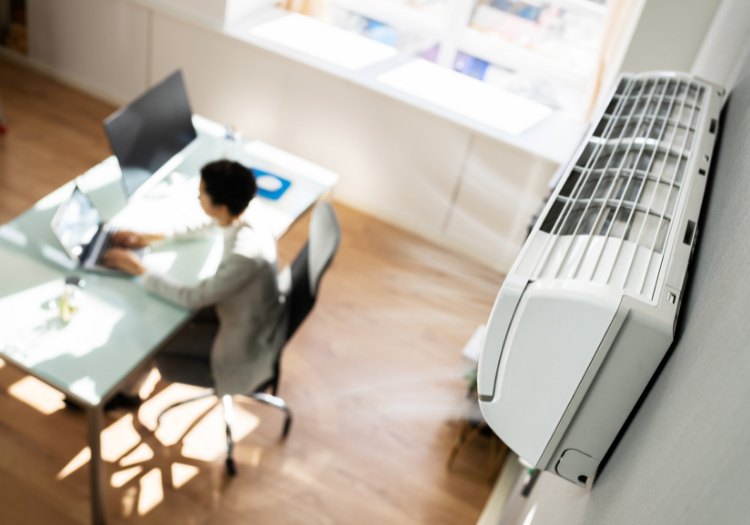 Ductless HVAC Systems: Office worker sits at desk while air conditioner runs.